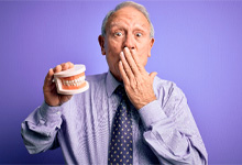 A man holding dentures in one hand while covering his mouth with the other