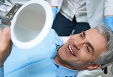 Happy patient using mirror to admire the results of his cosmetic dentistry treatment
