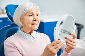 Senior female dental patient looking at smile in mirror