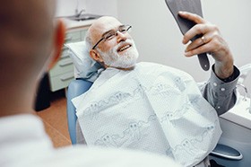 Senior man checking out his new implant denture at the dentist’s